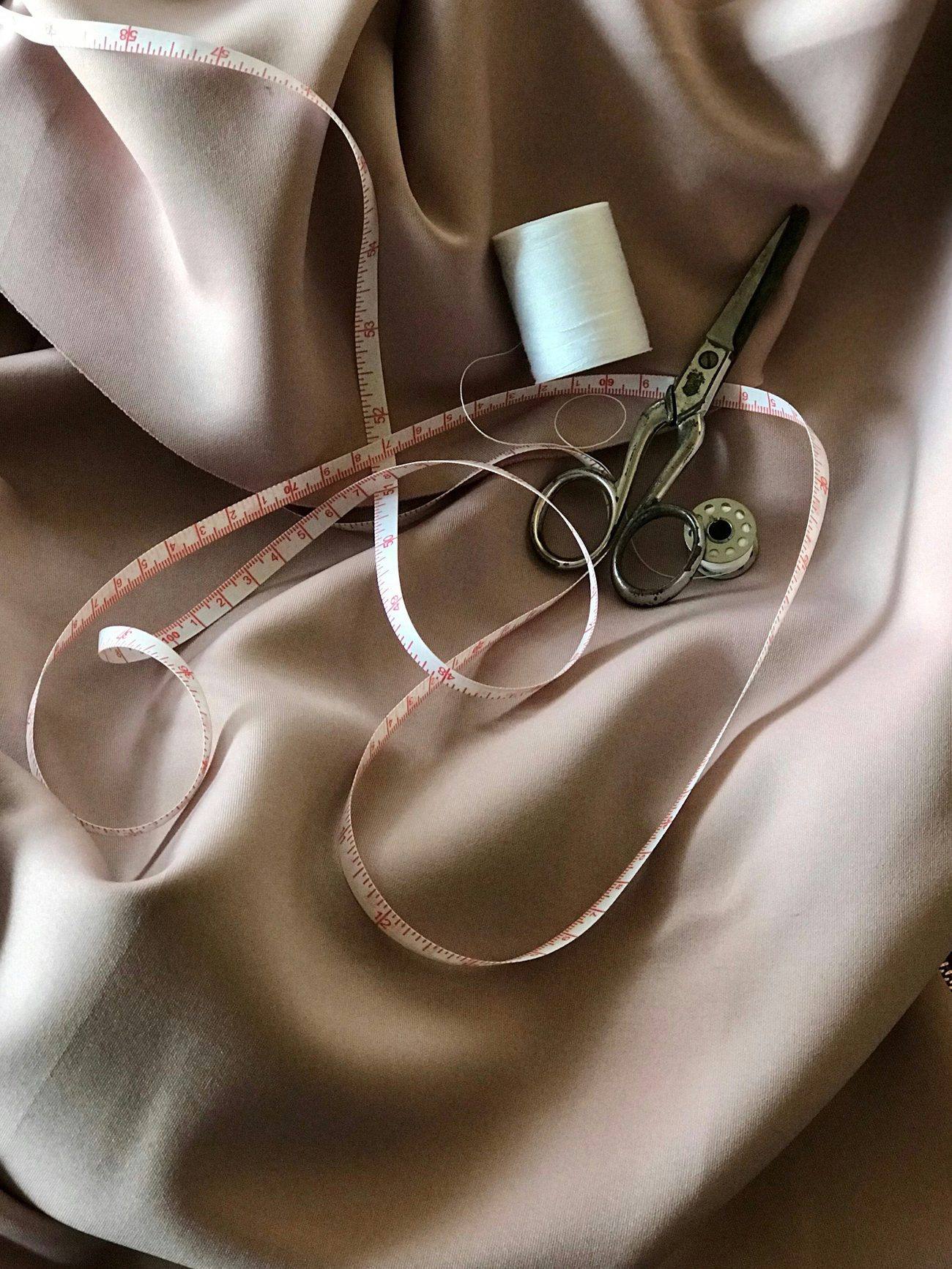 Tailoring tools — shears, measuring tape and thread resting on satin fabric