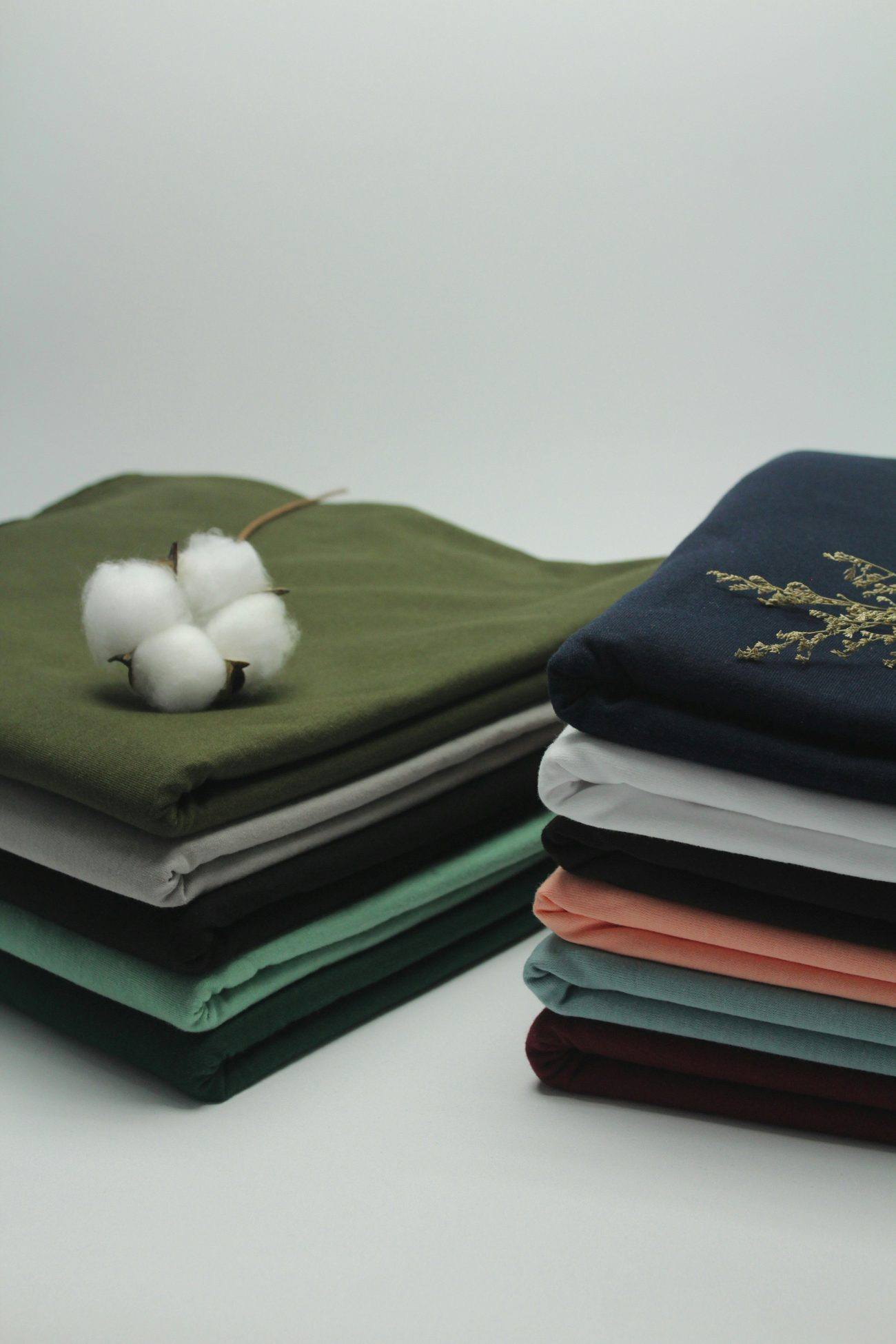 Neatly folded cotton garments in natural tones with raw cotton bolls